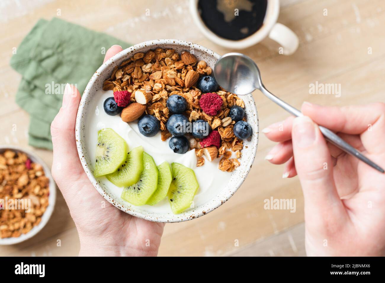 Female hands holding bowl of yogurt granola fruit bowl. Concept of clean eating, dieting, fitness food menu. Top view, selective focus Stock Photo