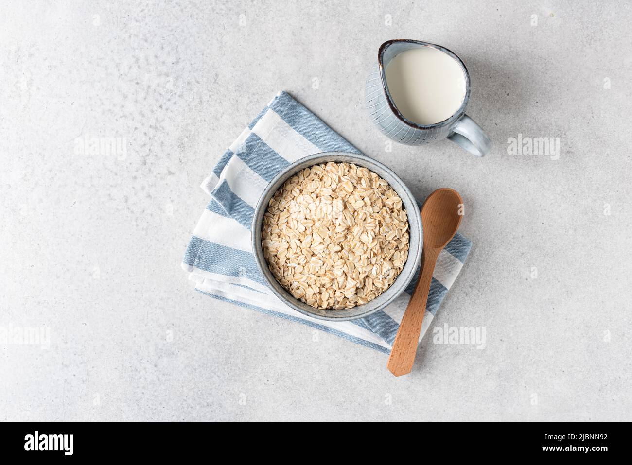 Oat flakes, rolled oats in bowl and jug of milk. Concept of healthy food. Grey concrete table background, top view Stock Photo