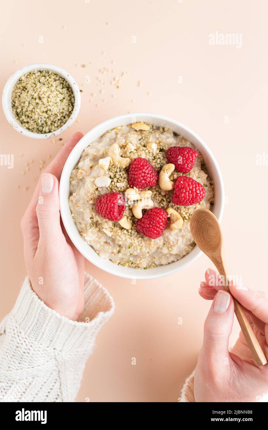 Eating oatmeal porridge with berries and seeds for breakfast. Concept of clean eating, dieting. Bowl of porridge oats in female hands. Top view copy s Stock Photo