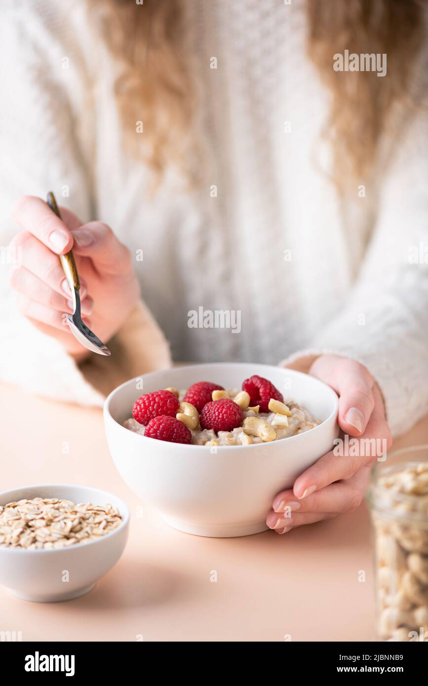 Bowl of oatmeal porridge with raspberries and cashew in female hands. Concept of clean eating, dieting, veganism Stock Photo