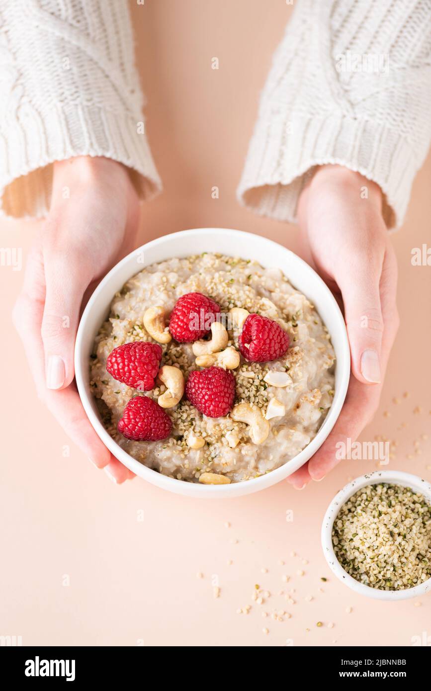 Oatmeal porridge bowl with berries and nuts in woman's hands. Concept of healthy vegan diet, clean eating, weight loss. Top view Stock Photo
