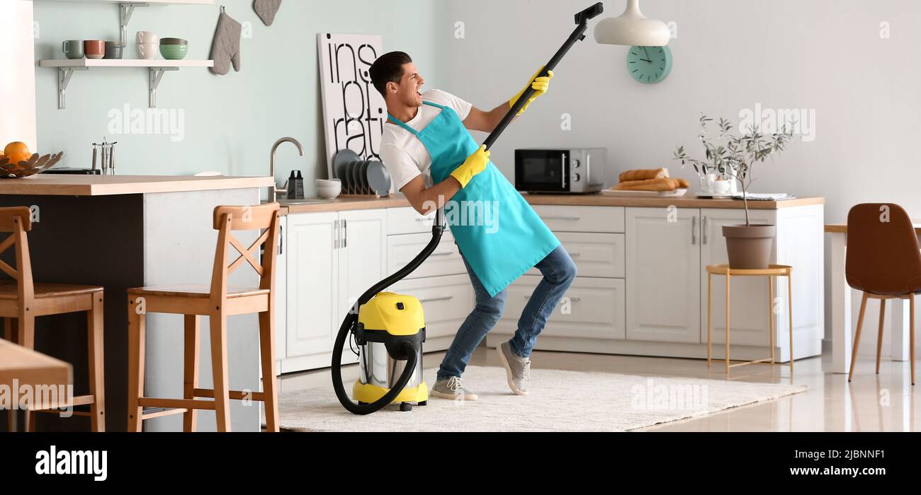 Young man having fun while vacuuming carpet in kitchen Stock Photo