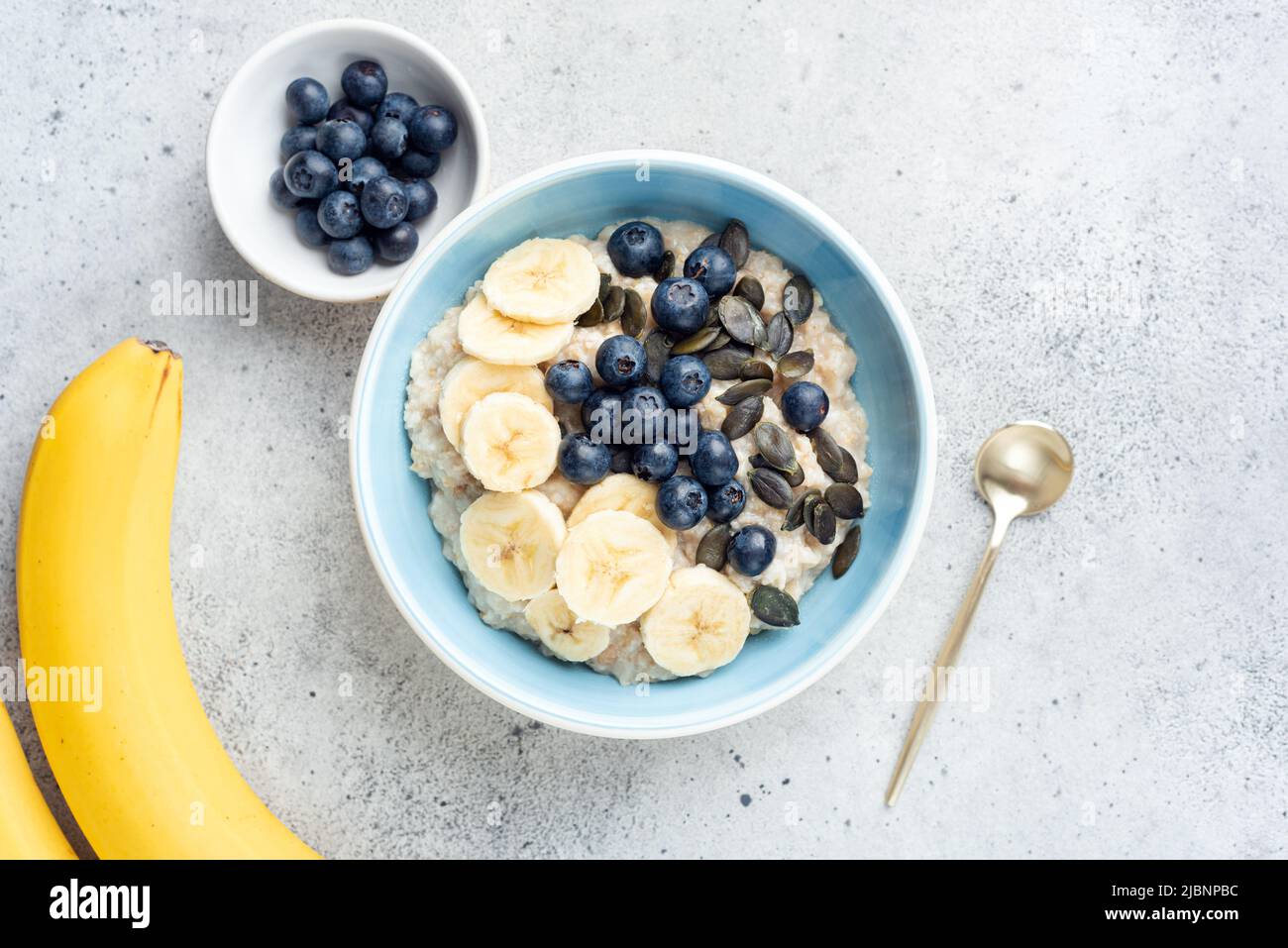 Oatmeal porridge with blueberries, bananas and pumpkin seeds on grey cocnrete background. Top view Stock Photo