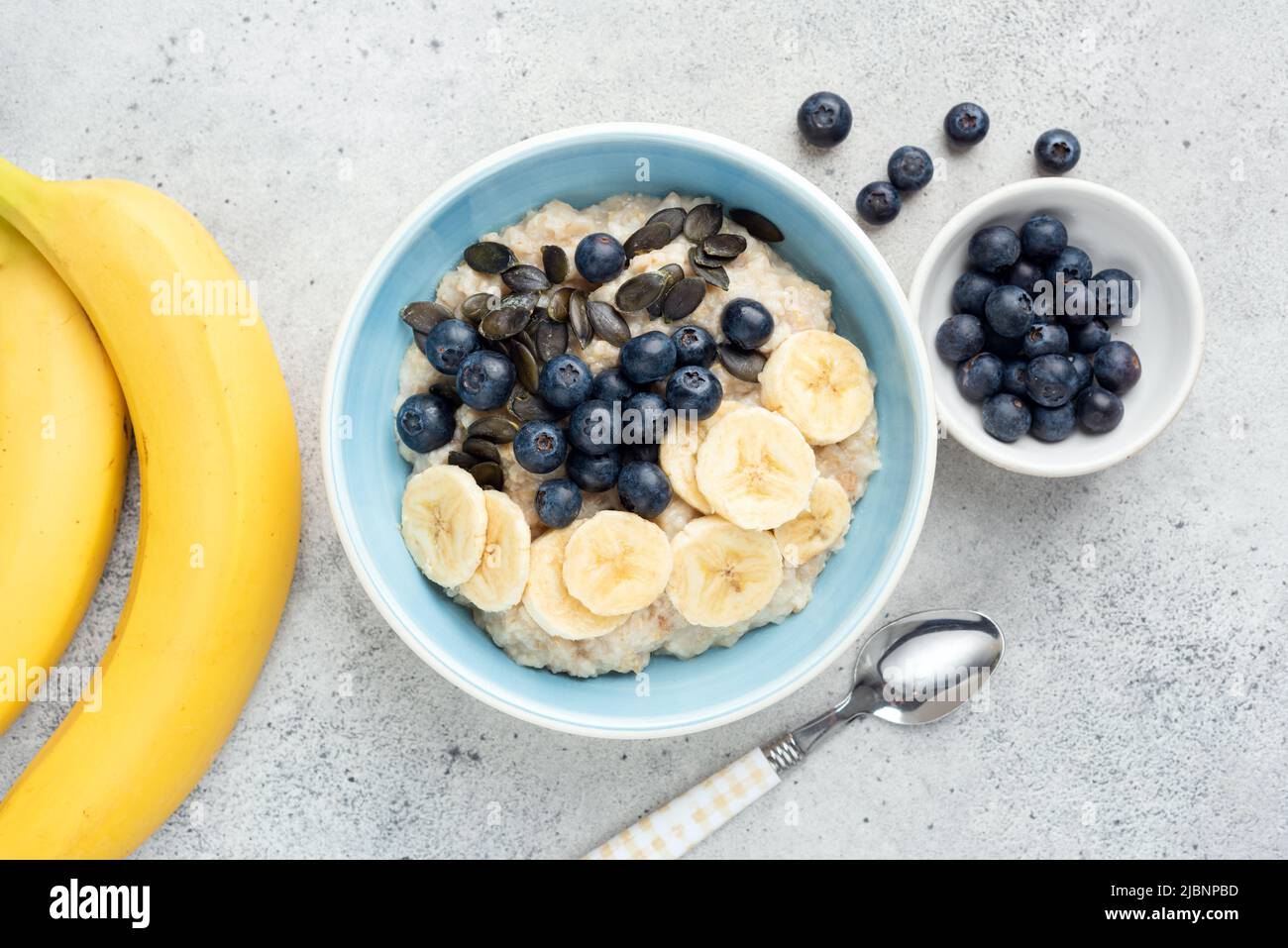 Oatmeal bowl with banana, blueberry and pumpkin seeds on grey cement background. Table top view Stock Photo