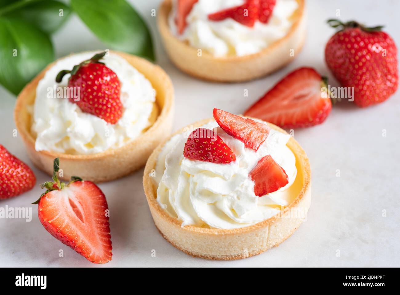 Shortcrust mini tarts with whipped cream and strawberries, closeup view Stock Photo