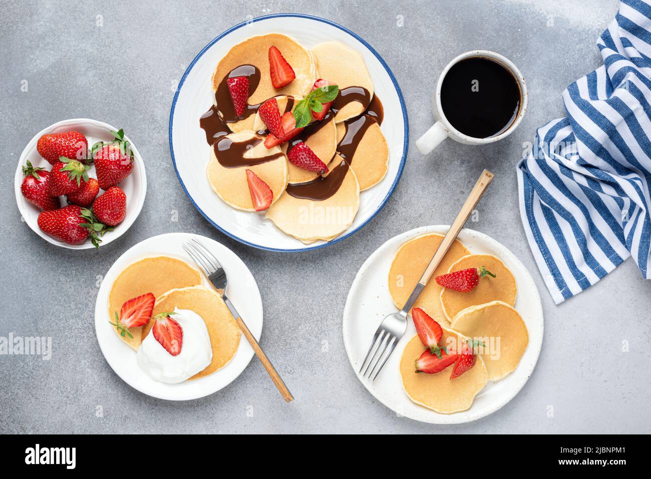 Pancakes served with fresh strawberries, chocolate syrup and yogurt, concrete table background. Top view. Family breakfast concept Stock Photo