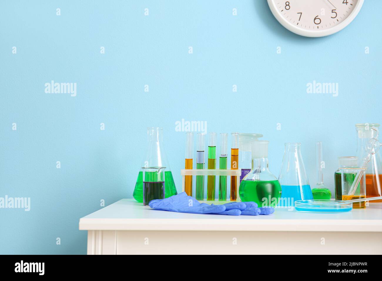 Different laboratory glassware with samples on table near blue wall