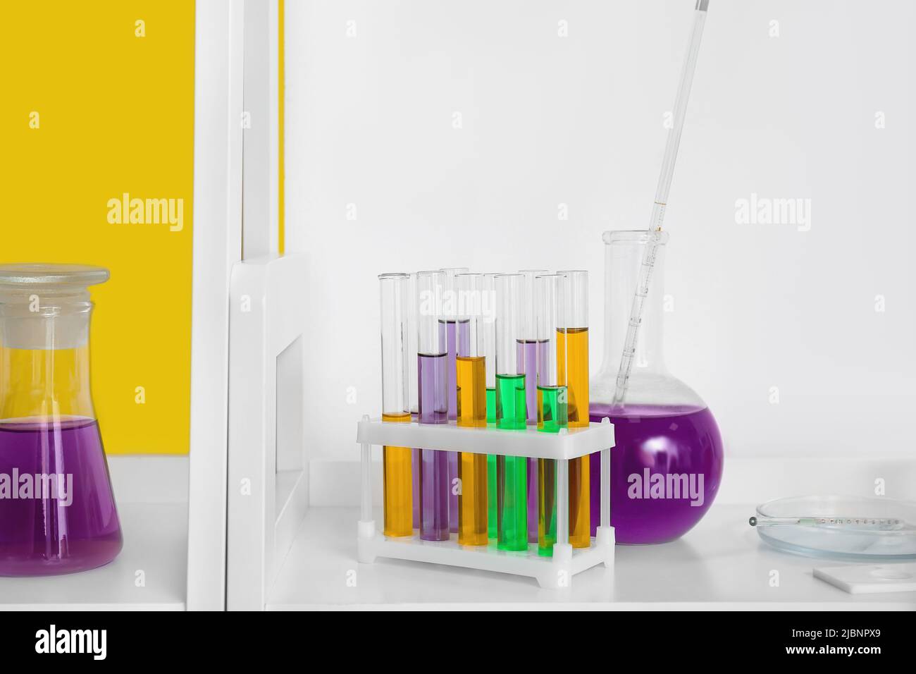 Laboratory glassware with samples on shelf near color wall Stock Photo