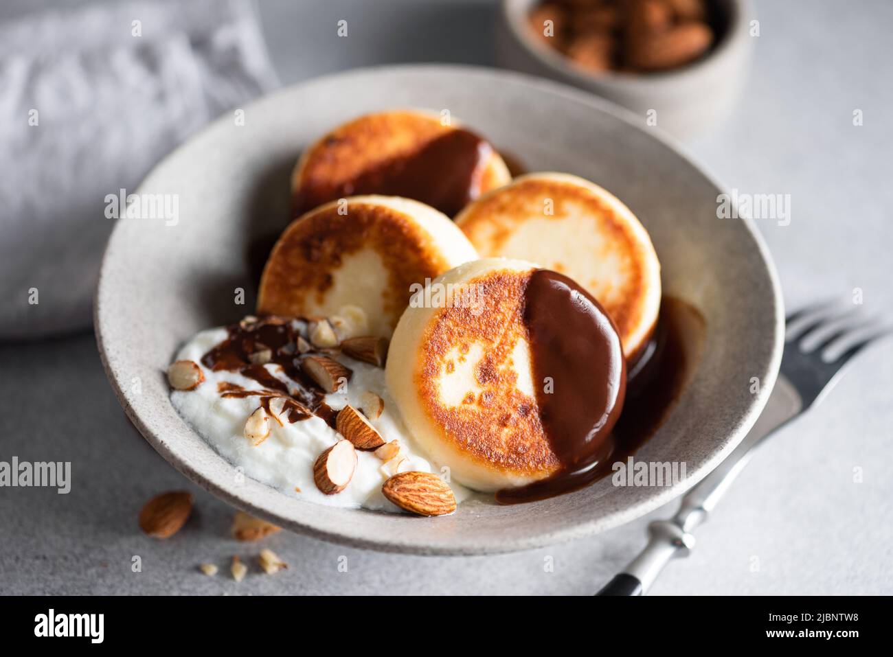 Cottage cheese fritters, syrniki served with chocolate, yogurt and almonds. Sweet breakfast food Stock Photo