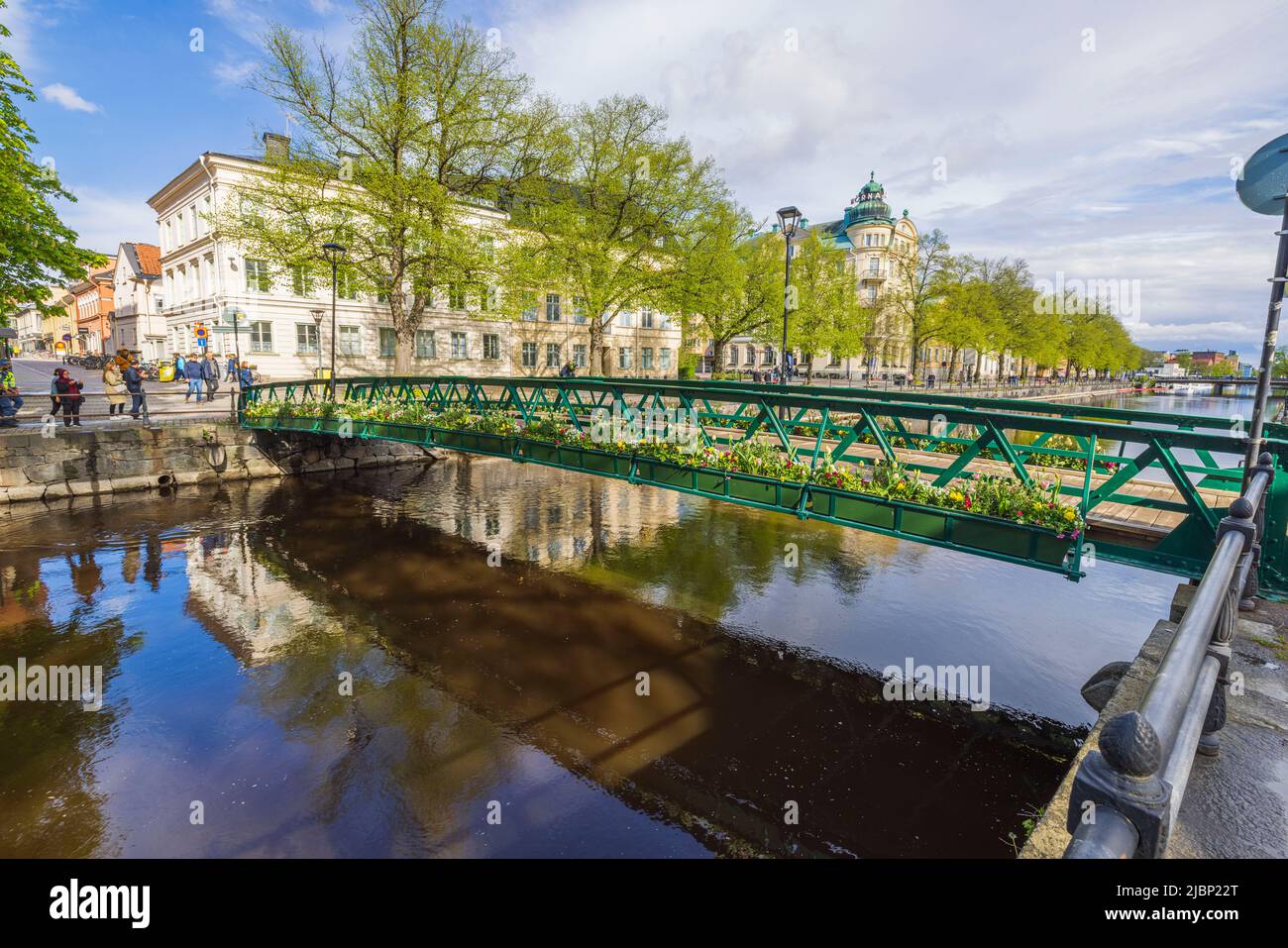 Lovely calming cityscape view. Cute bridge over small river decorated with flowers. Sweden. Uppsala. Stock Photo