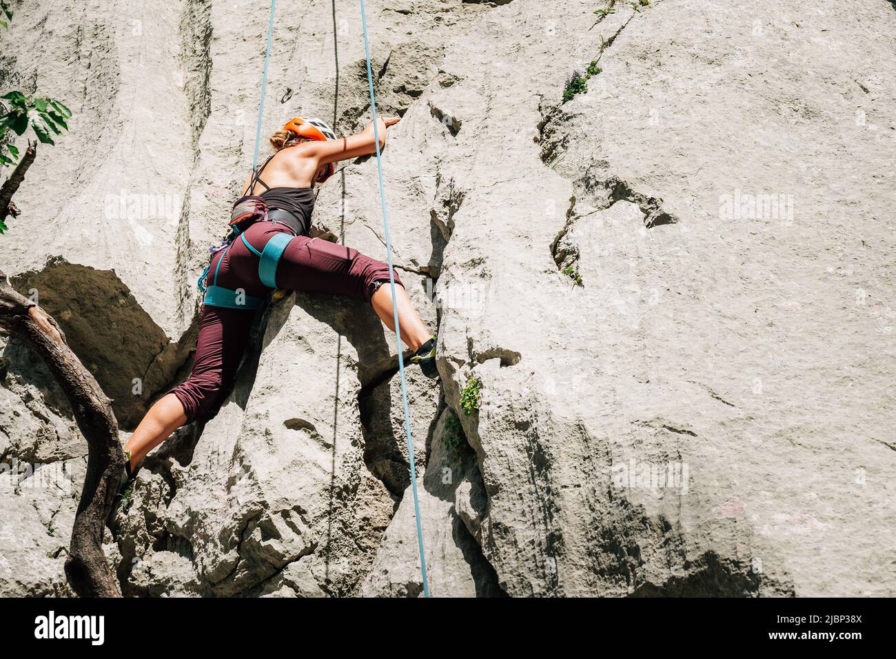 Athletic Woman in protective helmet and shoes climbing on cliff rock wall using top rope and climbing harness in Paklenica National park site in Croat Stock Photo