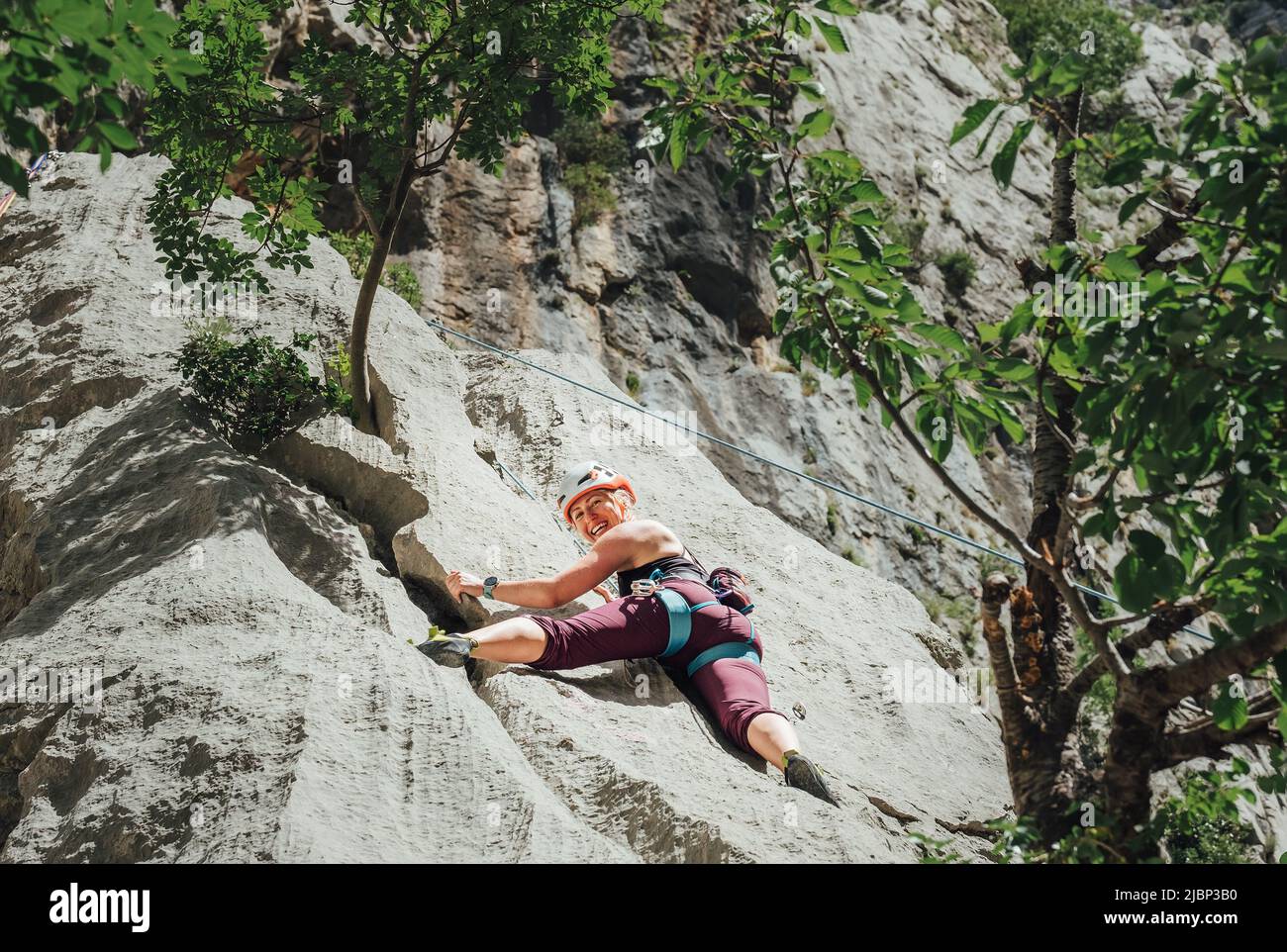 Smiling athletic woman in protective helmet climbing cliff rock wall using top rope and climbing harness in Paklenica National park site in Croatia. A Stock Photo