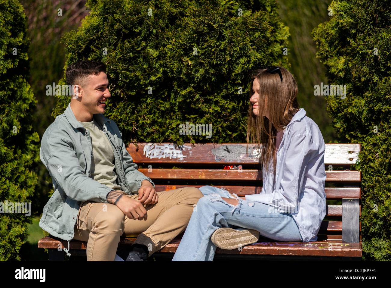 Two friends talking and laughing sitting on the bench in a park Stock