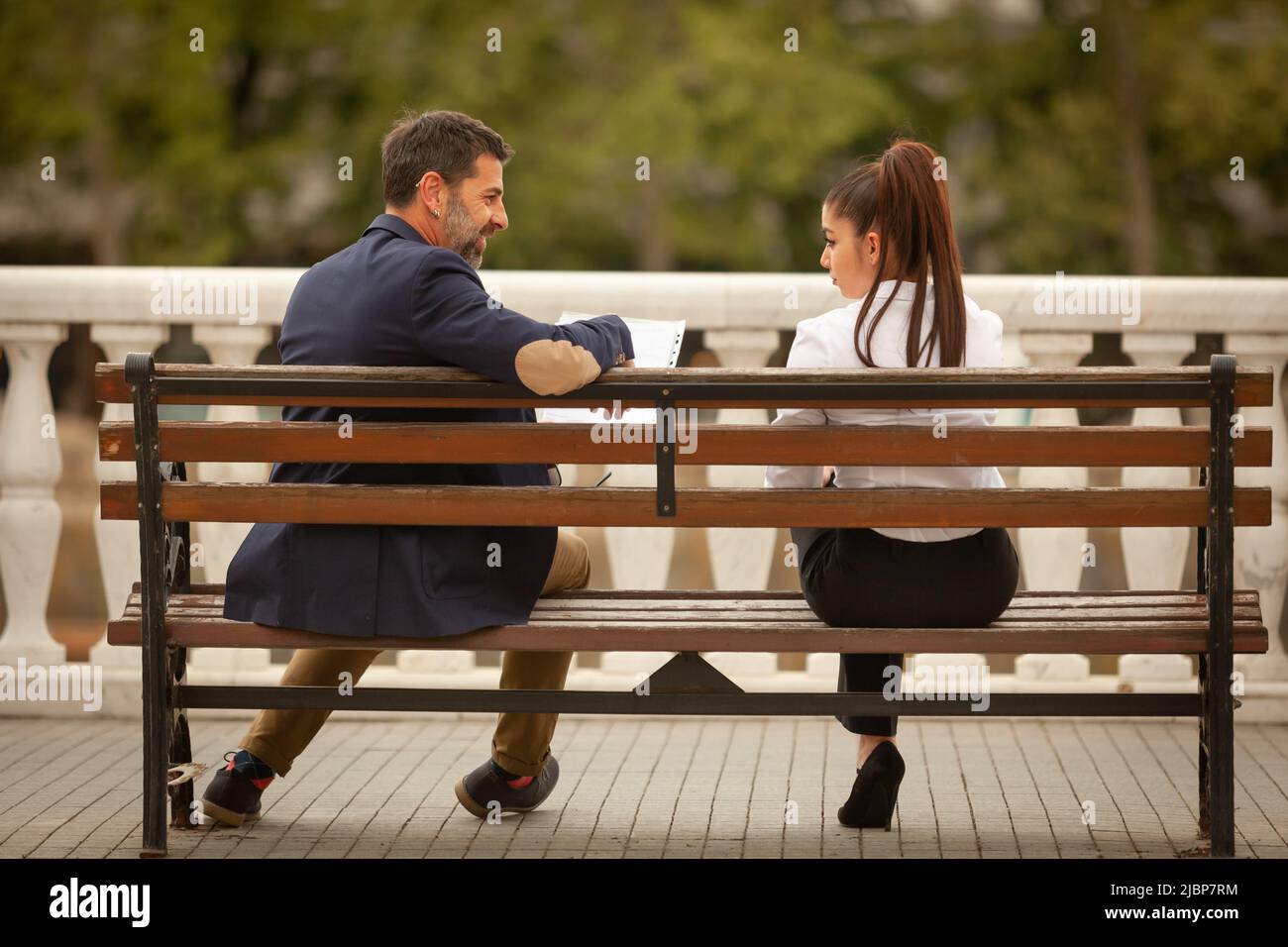 Two urban business people are sitting on the bench while talking about