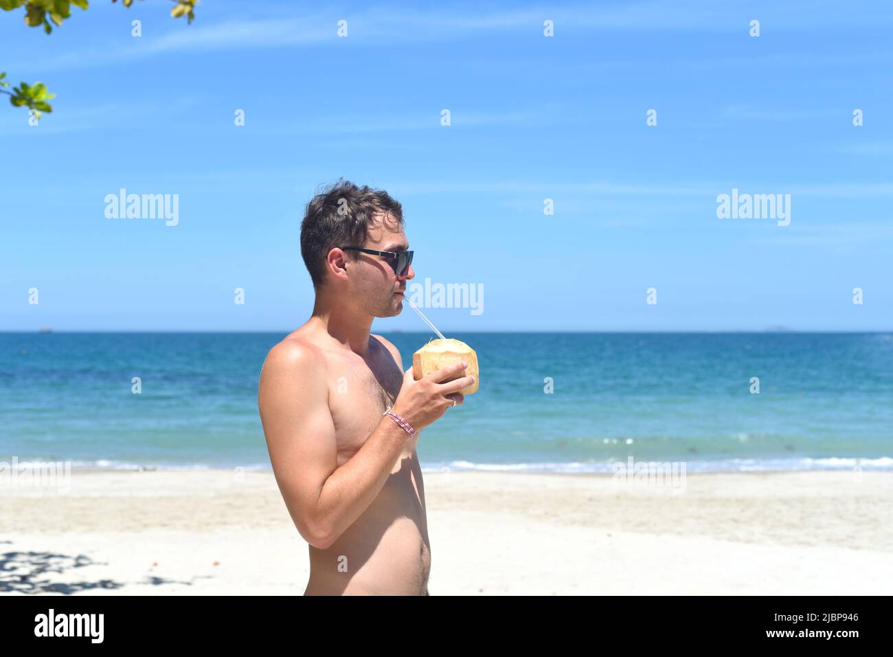 Young man drinking coconut on sandy beach Stock Photo