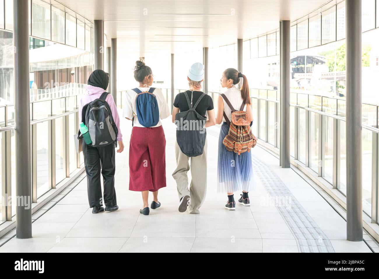 Group of multi-racial college student friends walking together in hall. Back view. Stock Photo