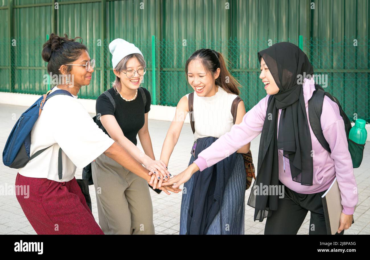 Group of happy multi-racial young female college students putting and stacking their hands together. Unity and teamwork concept. Stock Photo