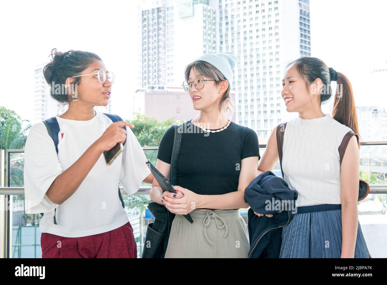 Three young multi-racial women friends smiling and talking to each other. Stock Photo