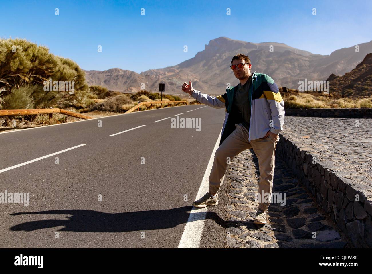 A hitchhiker stands near the road with a raised finger. Hitchhiking in