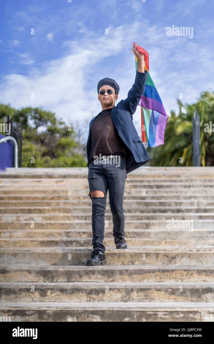 Lating gay male whit make-up on wearing fashionable hat holding lgbt flag. Concept of freedom and tolerance Stock Photo