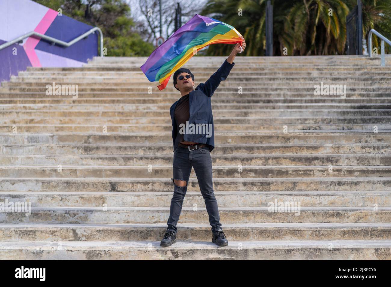 Lating gay male whit make-up on wearing fashionable hat holding lgbt flag. Concept of freedom and tolerance Stock Photo