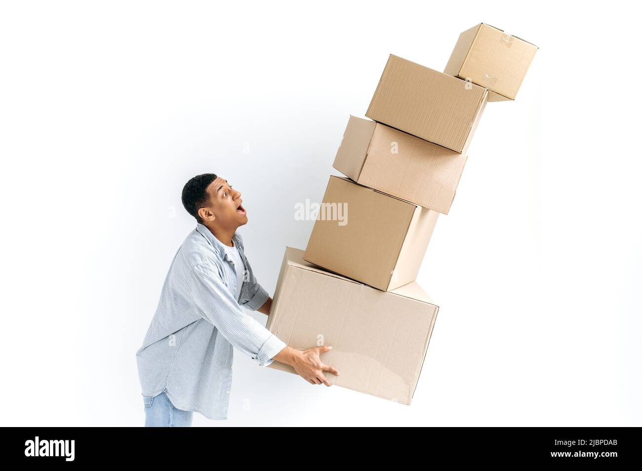 Stunned mixed race guy in casual stylish clothes, delivery man, standing over isolated white background, holding many cardboard boxes, delivering parcels, looking in amazement at falling boxes Stock Photo