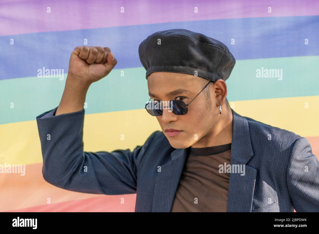 Portrait of a gay latin man with makeup wearing a fashionable hat on a rainbow background Stock Photo