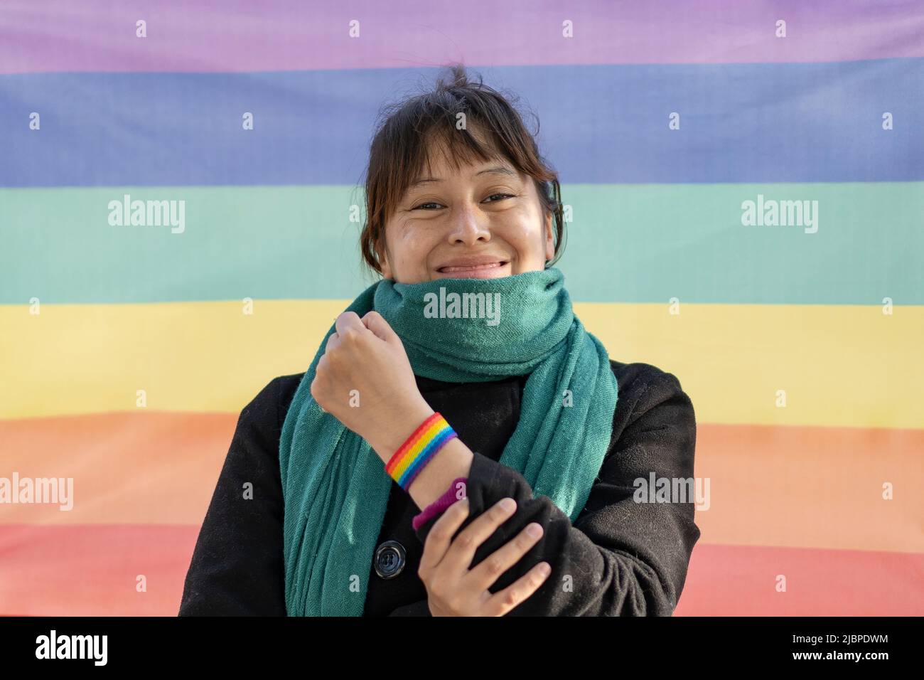 Portrait of a lesbian latin woman wearing lgbt wristband on a rainbow background Stock Photo