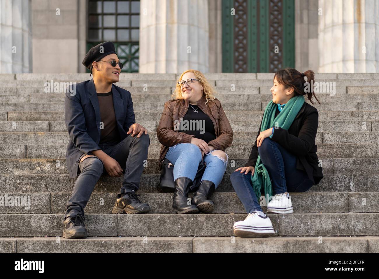 Multi ethnic group of friends sitting on some stairs having a good time chatting and laughing Stock Photo
