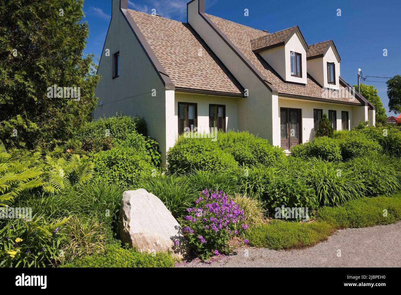 White and brown stucco cottage style home with landscaped front yard in