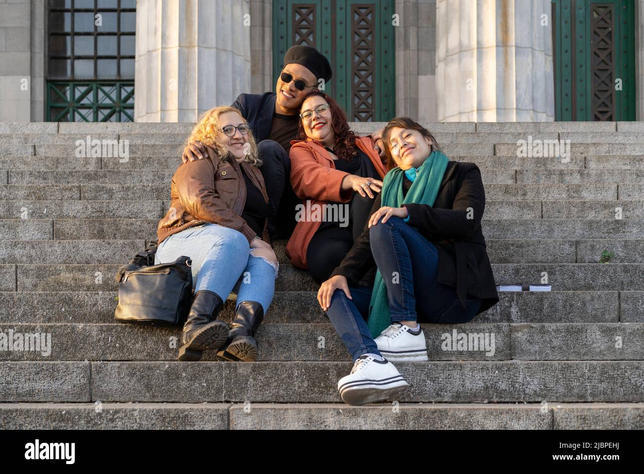Multi ethnic group of friends sitting on some stairs having a good time chatting and laughing Stock Photo
