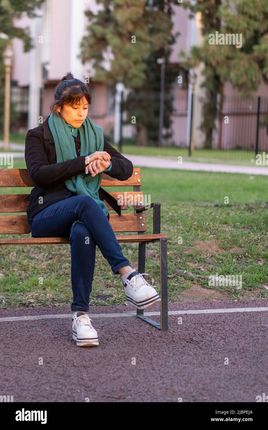 Latin woman sitting on a bench in a park looking at the time Stock Photo