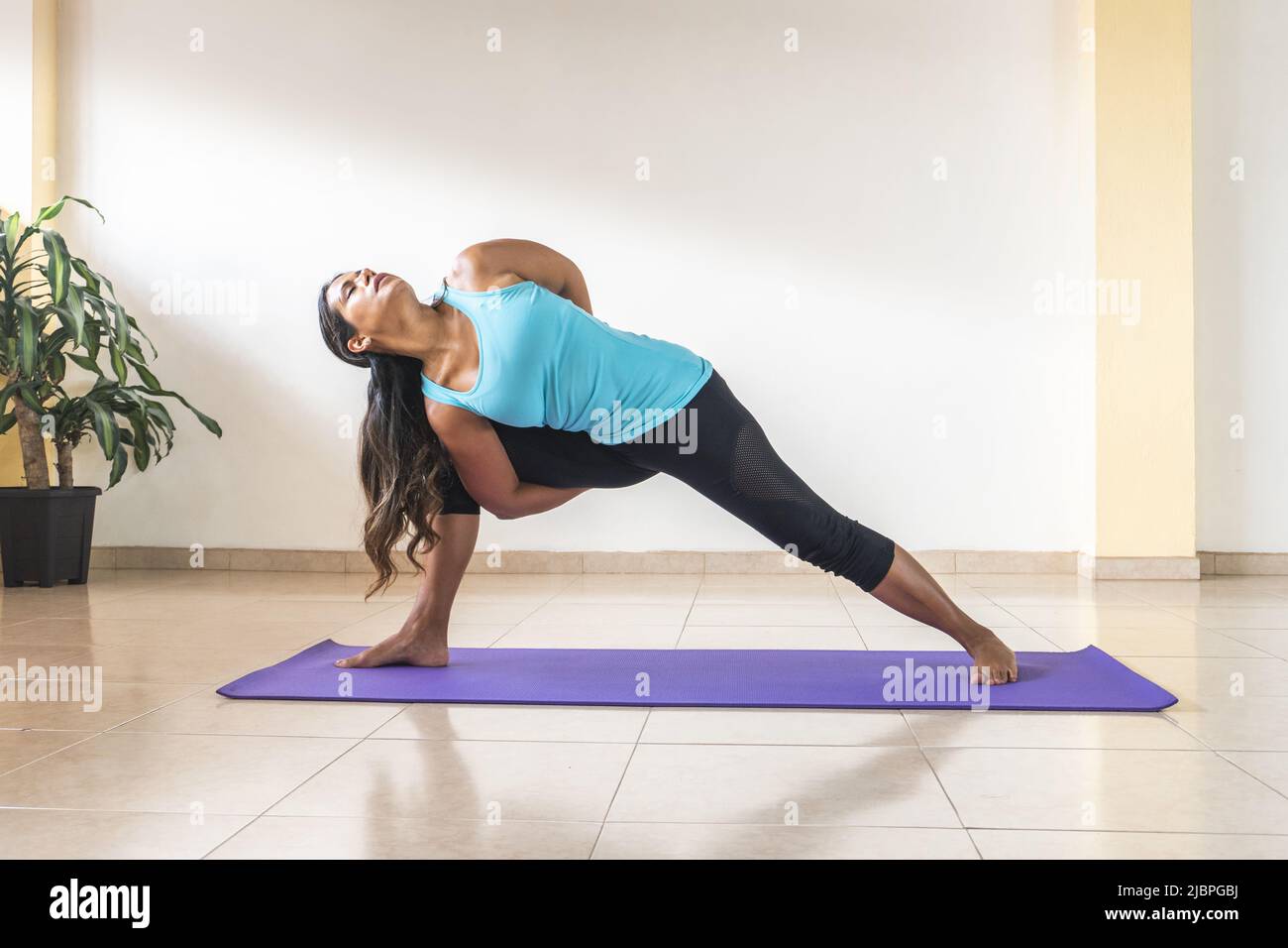 Brunette latin woman performing yoga poses, twisting triangle, Parivrtta baddha trikonasana on a mat Stock Photo
