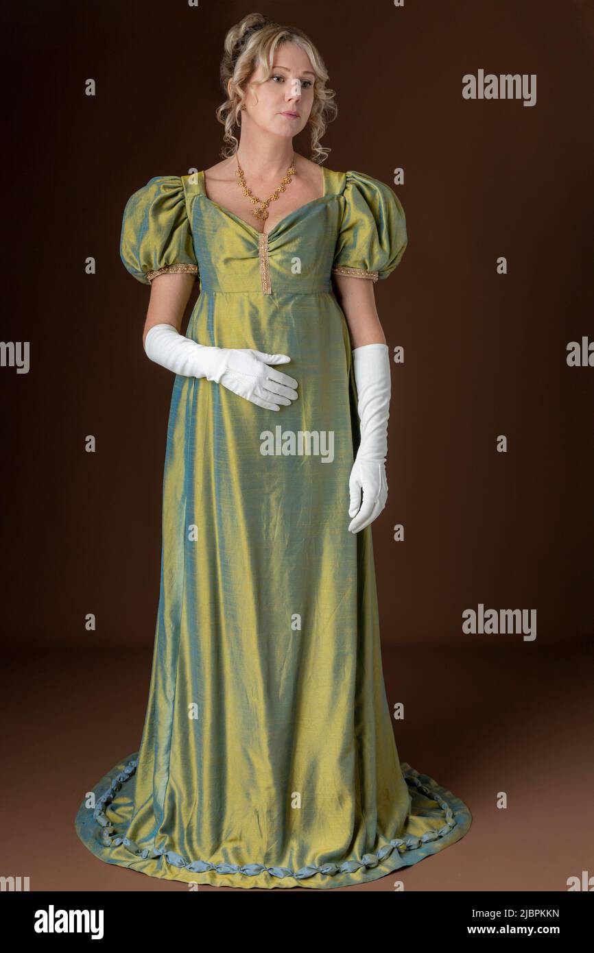 A Regency woman wearing a green shot silk dress and standing against a studio backdrop Stock Photo
