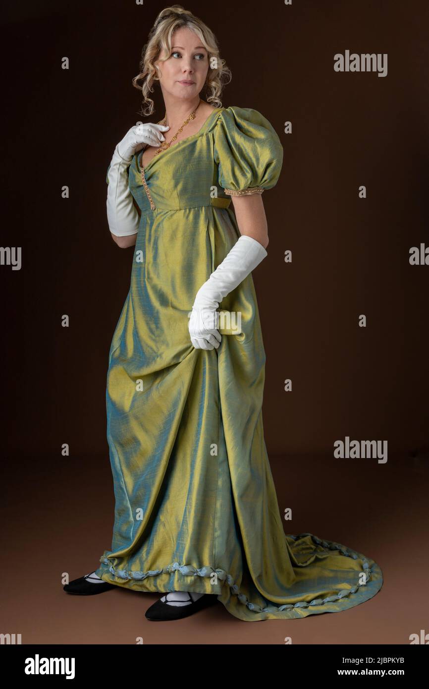A Regency woman wearing a green shot silk dress and standing against a studio backdrop Stock Photo