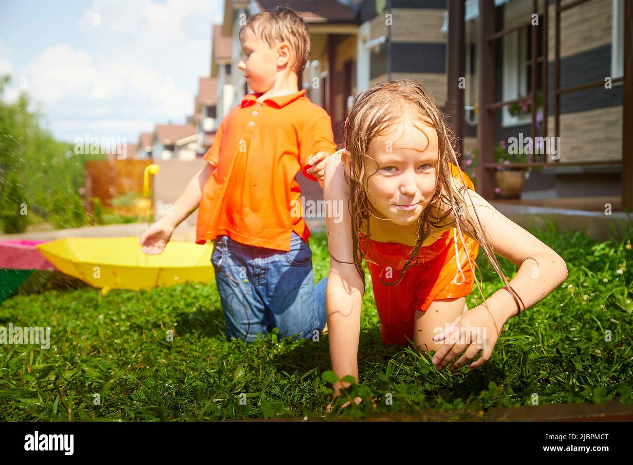 Children having fun and joy with an umbrella on green grass. Boy and girl having rest together. Brother and sister walk on nature Stock Photo