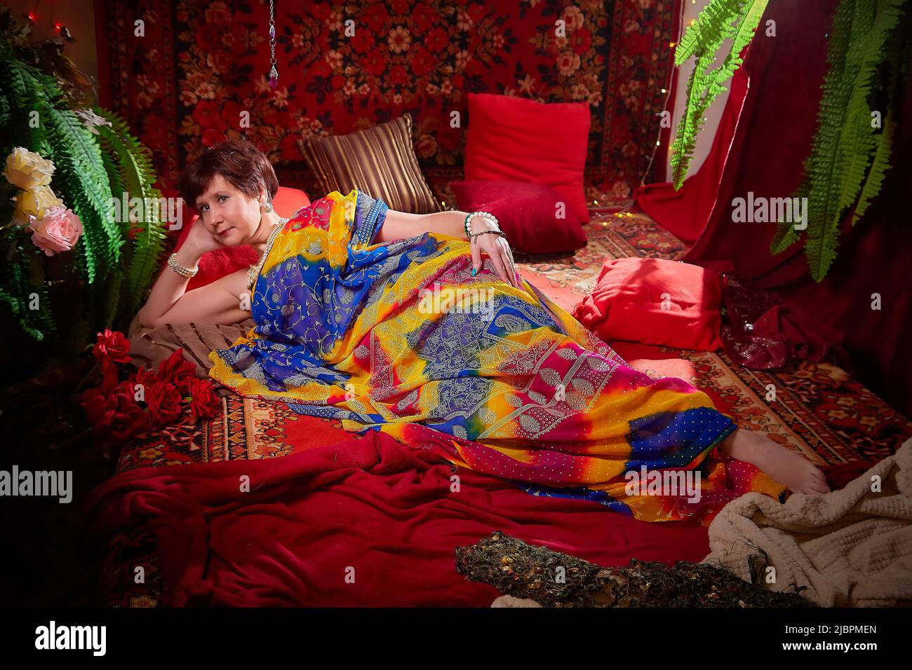 A beautiful European girl with short hair looking like an Arab woman in a red room in a harem. Photo shoot of an oriental style odalisque. A model Stock Photo