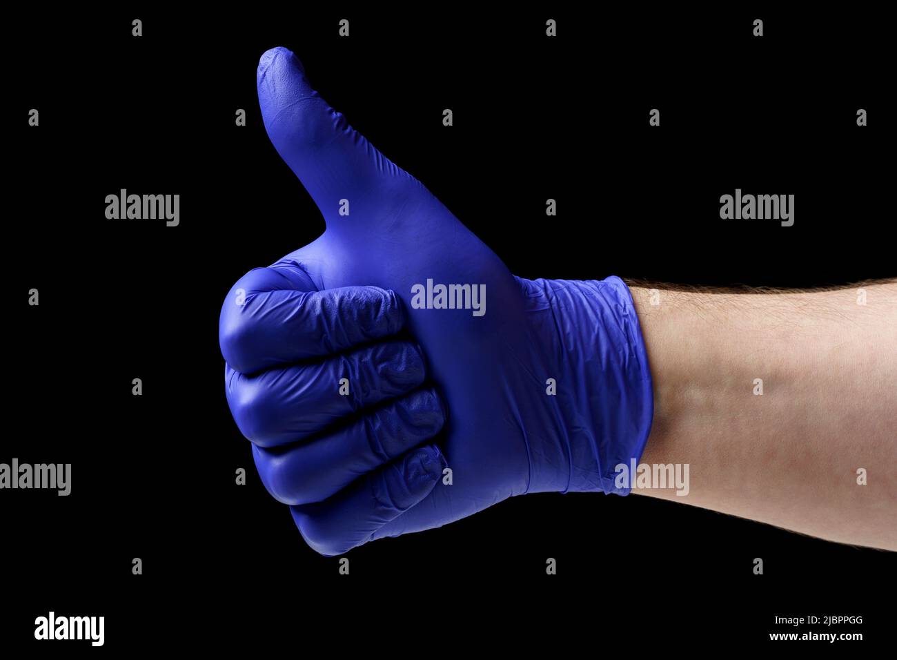 Man showing thumbs up. Close-up of a male hand in a blue latex glove on a black background. Stock Photo