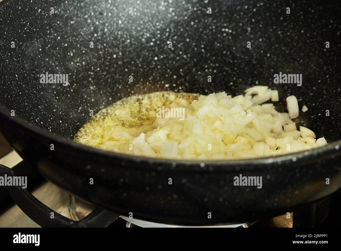 Finely chopped onions are fried in oil in frying pan on gas stove Stock