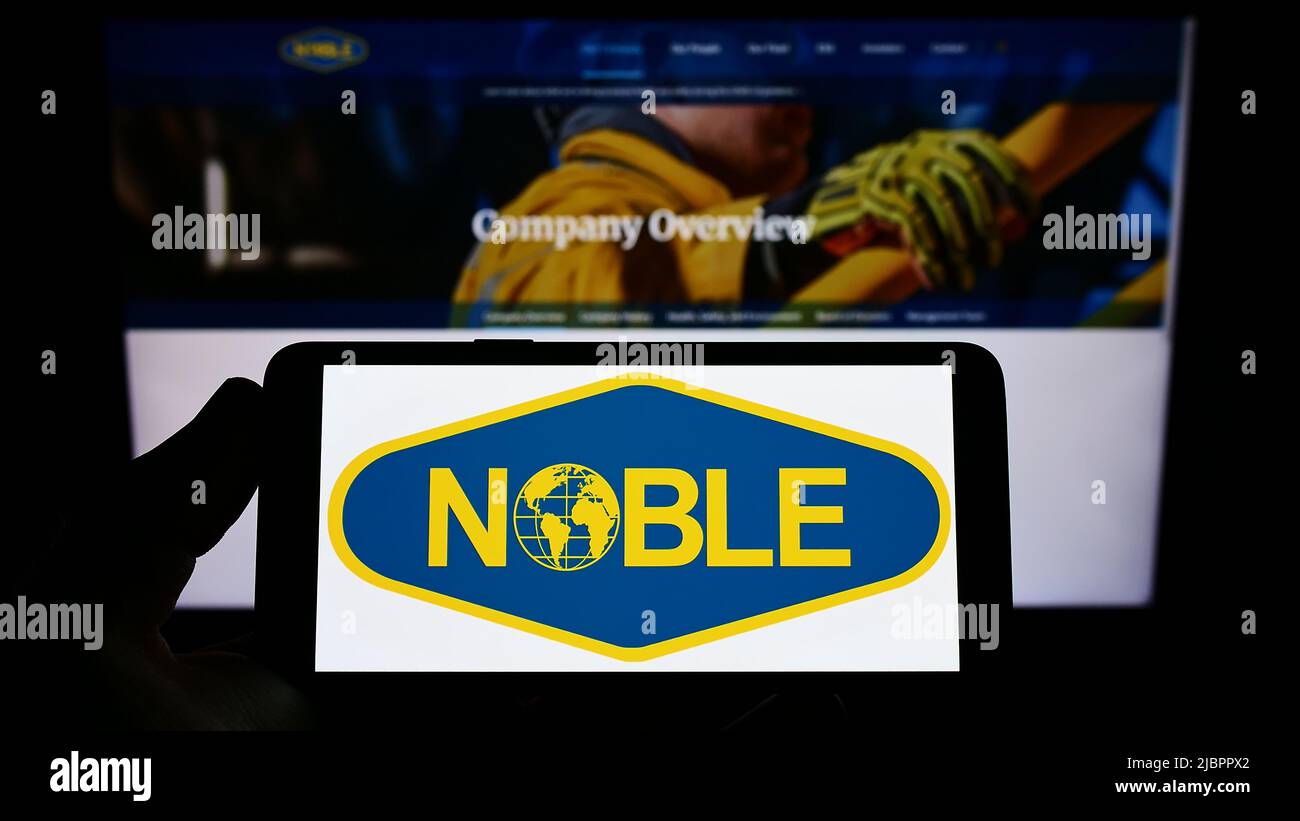 Person holding smartphone with logo of drilling company Noble Corporation plc on screen in front of website. Focus on phone display. Stock Photo