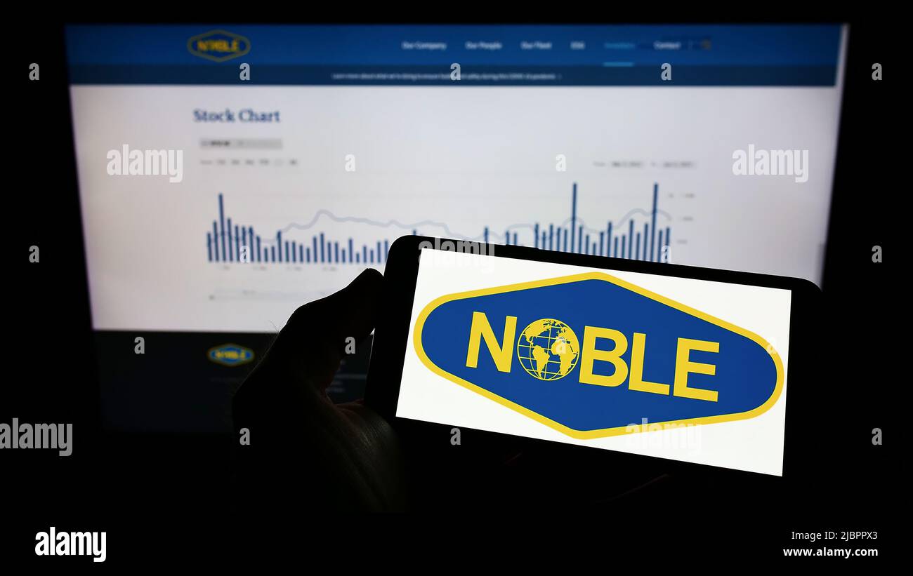Person holding mobile phone with logo of drilling company Noble Corporation plc on screen in front of business web page. Focus on phone display. Stock Photo