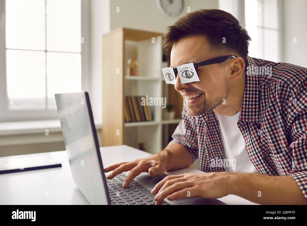Funny weird sleepy guy with paper stickers on eyes pretending to be working on laptop Stock Photo