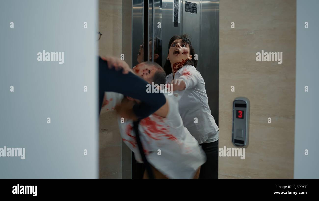 Businessman leaving office but starting to run when creepy brain-eating zombies come out of elevator. Man going home but horror looking bloody monsters get in his way and chase him downstairs. Stock Photo