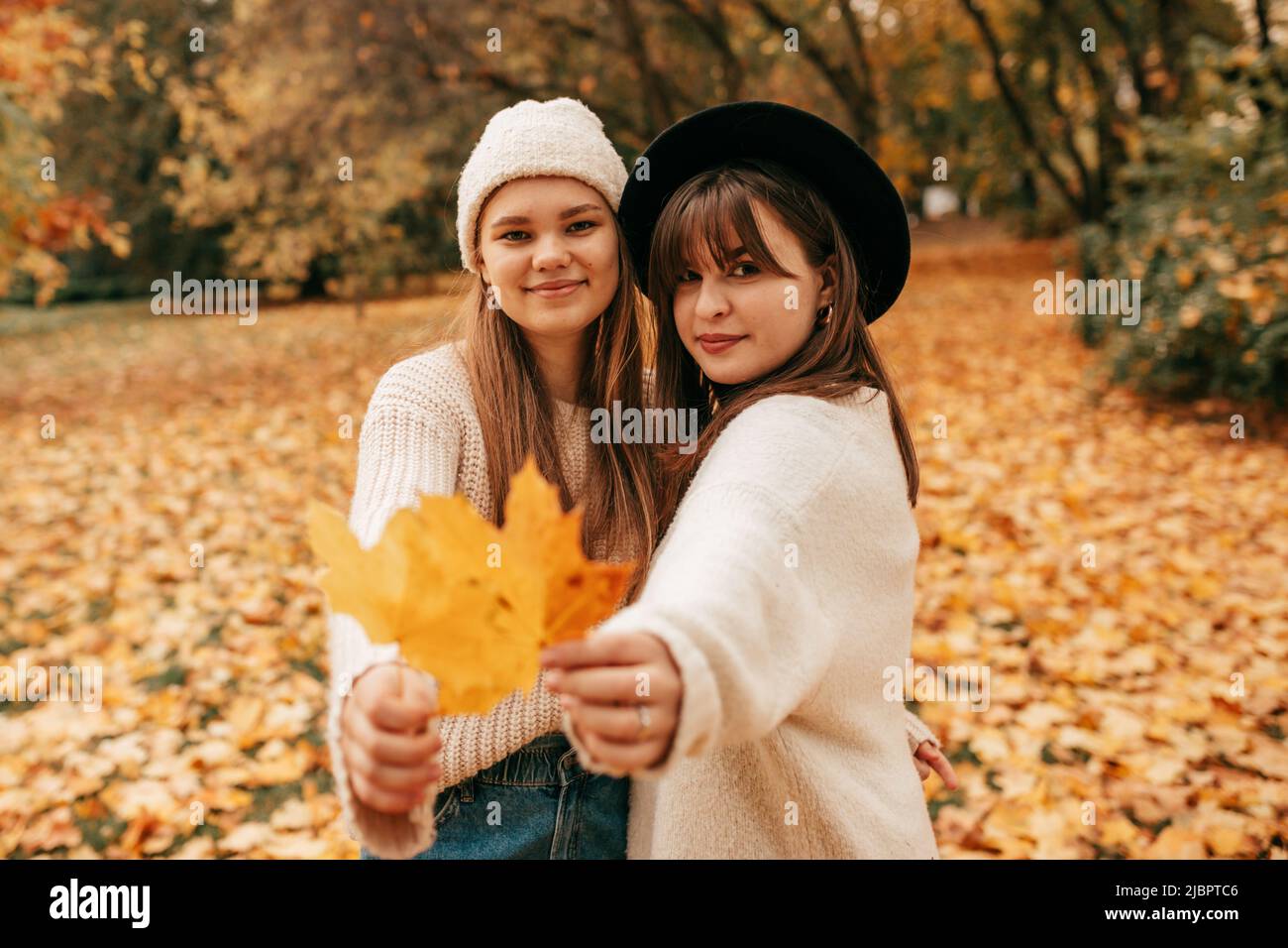 Beautiful young women enjoy their time in autumn park against background of bright trees. Golden autumn. Holidays. Fallen leaves. Female friendship Stock Photo