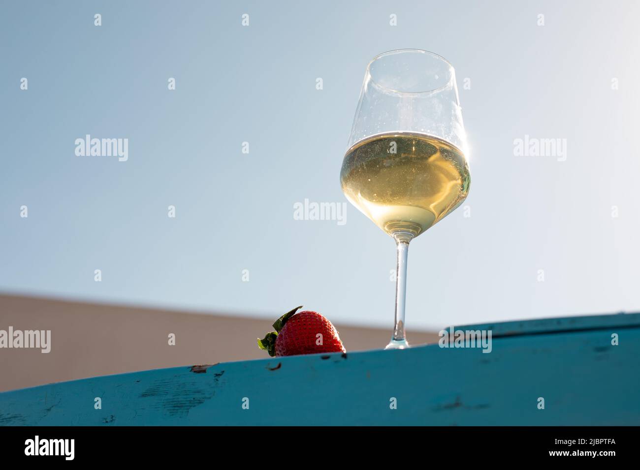 Close-up photo of wineglass with white yellow wine with strawberry. Vacation, romantic travelling and adventure concept. Stock Photo