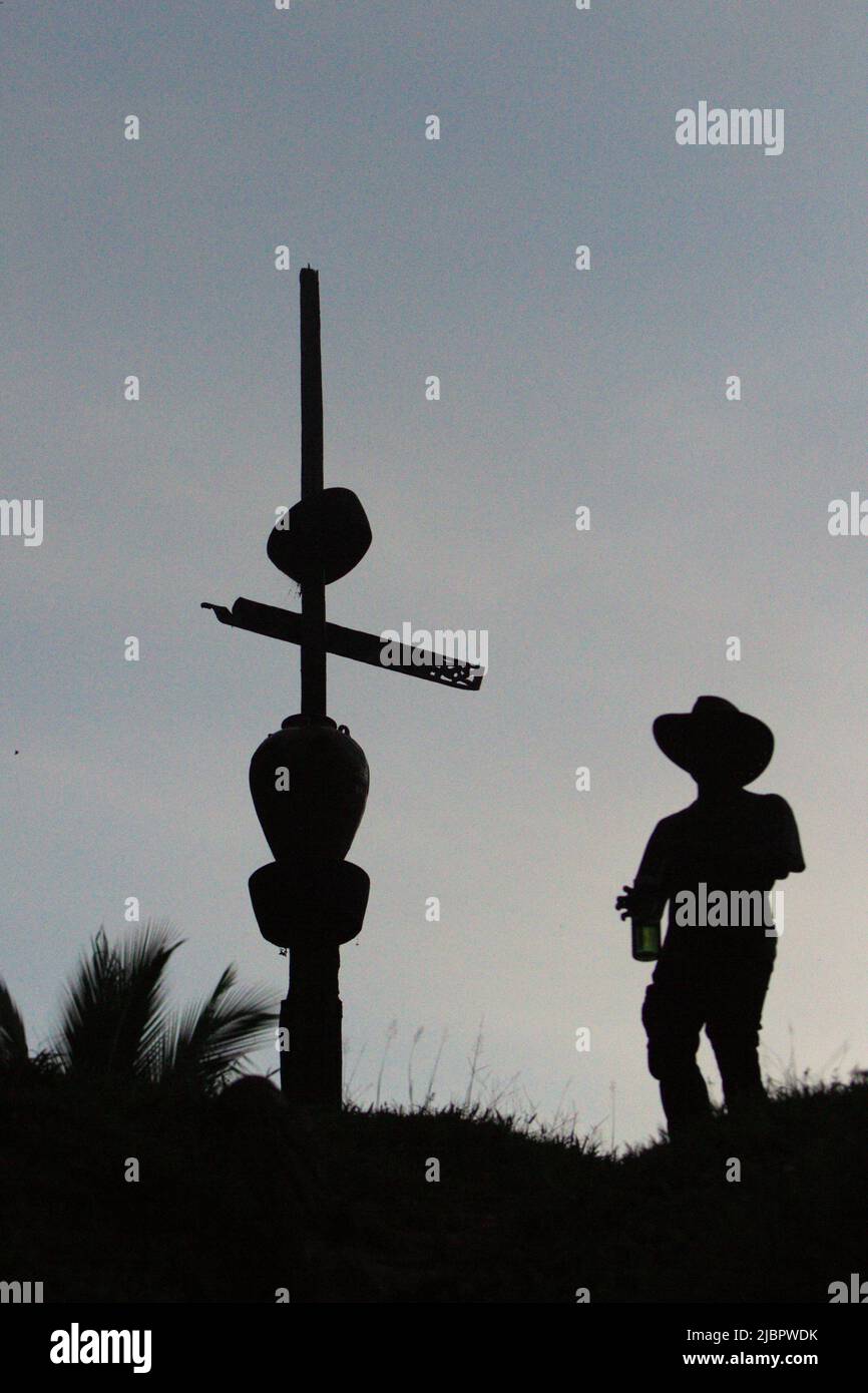 A facilitator of community-based ecotourism assessment wearing cowboy hat is silhouetted against bright sky as he is walking past a totem pole on the bank of Manday river in remote village of Nanga Raun in Kalis, Kapuas Hulu, West Kalimantan, Indonesia. 'The pole is a sign of the settlement area in the village, as well as a symbol to greet ancestor spirits,' said an elder in the village that is mostly inhabited by the indigenous Orung Da'an Dayak community. Stock Photo