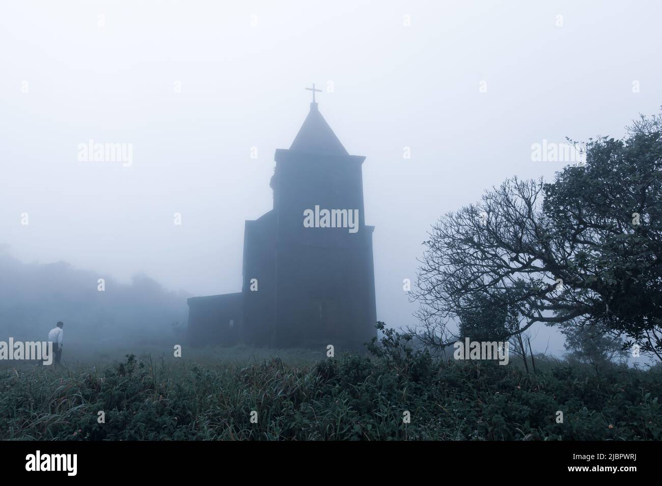 A man walks toward the abandoned Catholic church in fog, the church was built by the French in 1928. Damrei Mountains, Kampot, Cambodia. Stock Photo