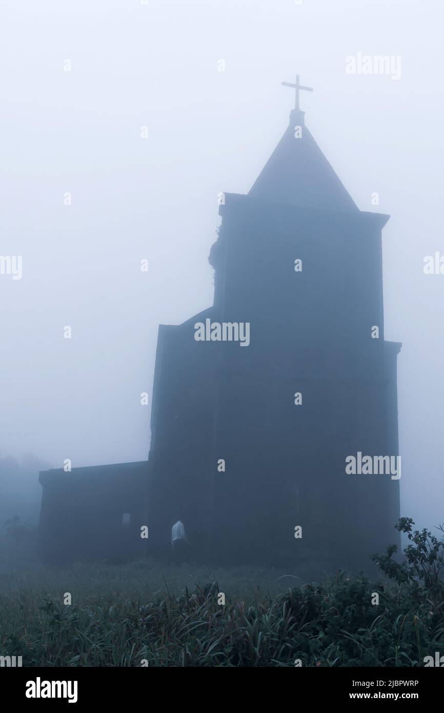 A man walks toward the abandoned Catholic church in fog, the church was built by the French in 1928. Damrei Mountains, Kampot, Cambodia. Stock Photo