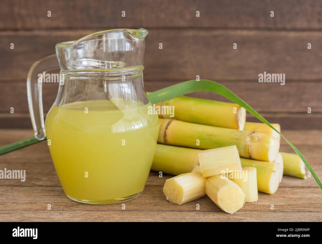 Fresh squeezed sugar cane juice in pitcher with cut pieces cane on