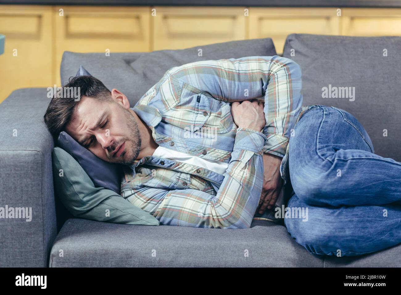 The sick man lying on the couch at home has severe abdominal pain Stock Photo